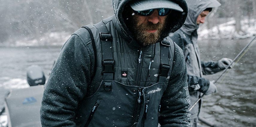 Man on a fishing boat wearing the torque heated vest, Great Lakes bibs, and buoy heavy duty hoodie